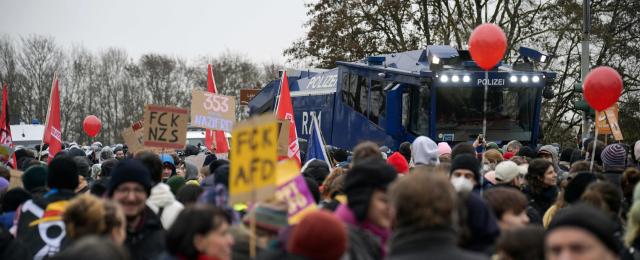 An armoured police vehicle stands next to demonstrators holding placards against farright politics during a protest against a two-day convention of far-right Alternative for Germany (AfD) party to establish its new youth organisation in Giessen, western Germany, on November 29, 2025. During the convention, Germany's AfD plans to establish its new youth organisation, to draft the organisation's statutes and elect its new leadership. The AfD's former youth organisation, Junge Alternative (Young Alternative), dissolved in spring 2025 after the party separated from it. Massive counter-protests from politicians and civil society have already been announced. The city announced that it intended to cordon off the entire area around the AfD event venue due to police security concerns. The anti-AfD protests are to be moved to the other side of the Lahn River. (Photo by Sascha Schuermann / AFP)