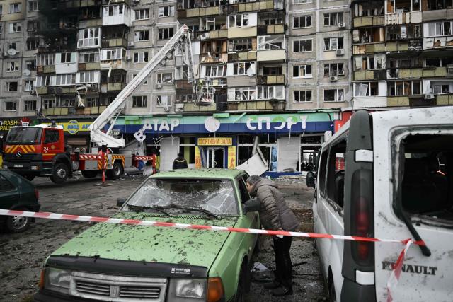TOPSHOT - A local resident inspects a damaged car in front of a damaged residential building following an air attack in Kyiv on November 29, 2025, amid the Russian invasion in Ukraine. A Russian drone attack targeted the Ukrainian capital in the early hours of November 29, 2025, killing one person and wounding seven, authorities in Kyiv said. (Photo by Genya SAVILOV / AFP)