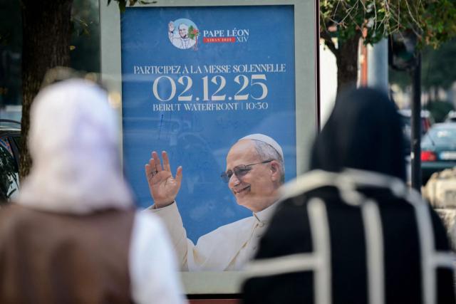 Women walk near a poster calling people to mass on the waterfront in Beirut on November 29, 2025, ahead of Pope Leo XIV's visit to Lebanon. Leo is due to arrive in Lebanon on November 30 for a three-day trip that includes an open-air mass at Beirut's waterfront that organisers expect to draw 120,000 people, as well as an interreligious meeting in the city centre. (Photo by Giuseppe CACACE / AFP)