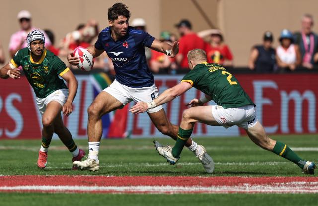 France's #08 Antoine Zeghdar (C) is tackled by South Africa's #02 Ryan Oosthuizen during the men's Dubai Sevens Rugby Union match between South Africa and France, at the The Sevens Stadium in Dubai on November 29, 2025. (Photo by Fadel SENNA / AFP)