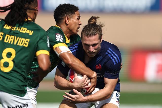 South Africa's #12 Shilton van Wyk (C) tackles France's #05 Stephen Parez-Edo Martin during the men's Dubai Sevens Rugby Union match between South Africa and France, at the The Sevens Stadium in Dubai on November 29, 2025. (Photo by Fadel SENNA / AFP)