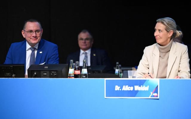 Co-leaders of the far-right Alternative for Germany (AfD) party Tino Chrupalla (L) and Alice Weidel sit on the podium during a two-day convention of far-right Alternative for Germany (AfD) party to establish its new youth organisation at the exhibition halls in Giessen, western Germany, on November 29, 2025. A meeting set to launch the new youth wing of the far-right Alternative for Germany (AfD) was delayed on November 29 as thousands of protestors blocked access to the event venue. Thousands of anti-AfD protestors began descending on the town of Giessen from early morning, with police also out in force. One of the protest organisations, "Resist", said that it blocked several routes towards the AfD meeting and had gathered 15,000 people. (Photo by Kirill KUDRYAVTSEV / AFP)