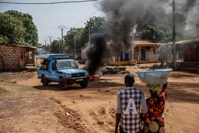 TOPSHOT - A Guinea Bissau Police patrol car speeds past burning tyres as a couple approaches the scene on Novmeber 29, 2025. (Photo by Patrick MEINHARDT / AFP)