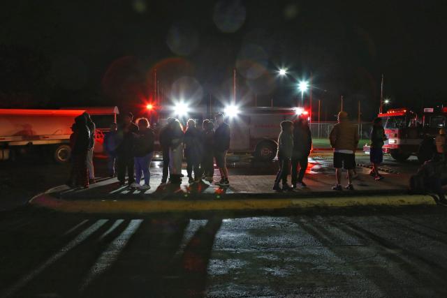 People stand stand near firefighters vehicles after a house where clandestine fireworks were being manufacture exploded leaving three people dead and six injured, in the municipality of Pesqueria, Nuevo Leon state, Mexico, on November 28, 2025. (Photo by Julio Cesar AGUILAR / AFP)