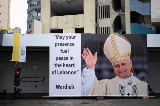 A gas station employee sets a Vatican flag next to a large banner of Pope Leo XIV in Beirut on November 29, 2025. Militant group Hezbollah on November 29 urged Pope Leo XIV to reject Israeli "injustice and aggression" against Lebanon, in a message to the pontiff who arrives in Beirut this weekend. (Photo by Jewel SAMAD / AFP)