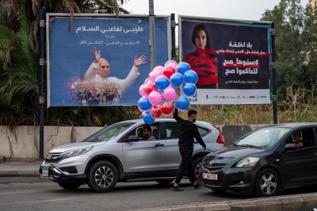 A man selling balloons looks for customers on a street near a billboard with a picture of Pope Leo XIV in Beirut on November 29, 2025. Militant group Hezbollah on November 29 urged Pope Leo XIV to reject Israeli "injustice and aggression" against Lebanon, in a message to the pontiff who arrives in Beirut this weekend. (Photo by Jewel SAMAD / AFP)