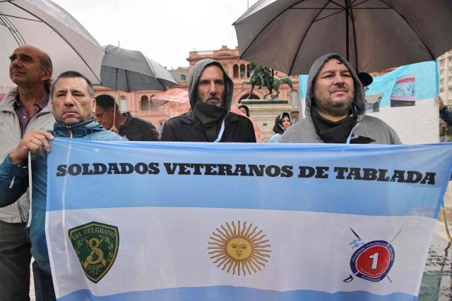 Defenders of convicted perpetrators of genocide holding a flag that reads “Veteran Soldiers of Tablada” demonstrate in Plaza de Mayo in Buenos Aires, on November 29, 2025, wearing a black scarf instead of the traditional white one of the Human Rights activists Madres and Abuelas de Plaza de Mayo. (Photo by Emiliano Lasalvia / AFP)