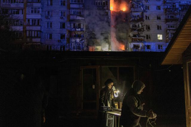 People walk past damaged shops in front of a residential building on fire following a Russian drone attack on the city of Vyshhorod, in the Kyiv region early on November 30, 2025, amid the Russian invasion of Ukraine. A Russian drone attack has killed one person and wounded 11 on the outskirts of the Ukrainian capital, the regional governor said on November 30. (Photo by Roman PILIPEY / AFP)