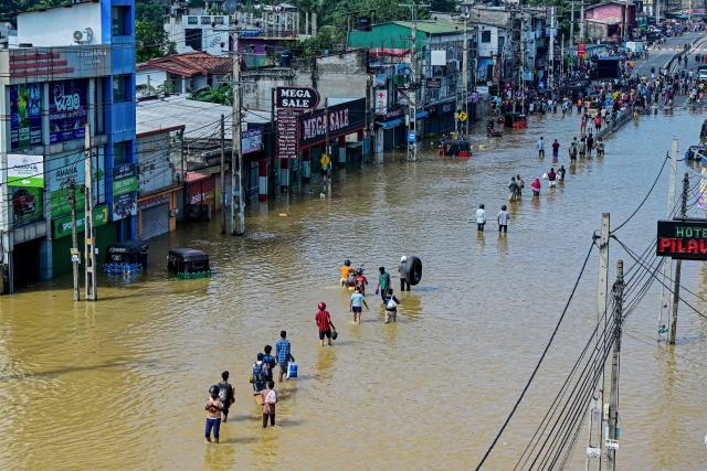 People wade through a flooded street after heavy rainfall in Wellampitiya on the outskirts of Colombo on November 30, 2025. Sri Lankan authorities battled rising floodwaters in parts of the capital on November 30 after a powerful cyclone left a trail of destruction, killing at least 159 people across the country. (Photo by Ishara S. KODIKARA / AFP)