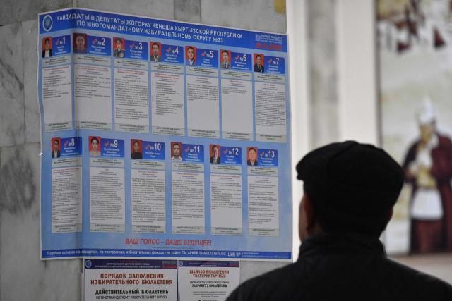 A man looks at an information placard bearing portraits of candidates at a polling station during Kyrgyzstan's snap parliamentary elections in Bishkek on November 30, 2025. (Photo by Vyacheslav OSELEDKO / AFP)