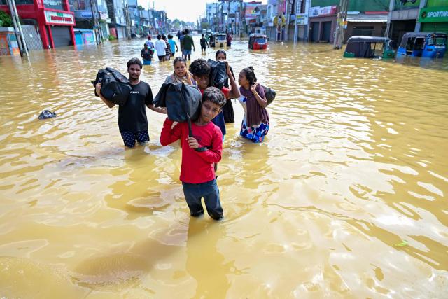 TOPSHOT - People with their belongings wade through a flooded street after heavy rainfall in Wellampitiya on the outskirts of Colombo on November 30, 2025. Sri Lankan authorities battled rising floodwaters in parts of the capital on November 30 after the powerful Cyclone Ditwah left a trail of destruction, killing at least 159 people across the country. (Photo by Ishara S. KODIKARA / AFP)