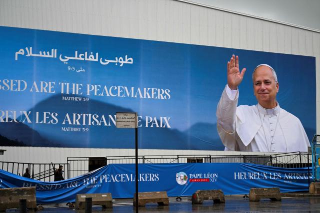 Workers carry a structure past a large banner featuring a picture of Pope Leo XIV as preparations are underway for a mass in Beirut on November 30, 2025. On his first overseas trip since being elected leader of the world’s 1.4 billion Catholics, Leo is scheduled to arrive in Lebanon on November 30 with a message of peace for the crisis-mired nation, after wrapping up a four-day visit to Turkey. (Photo by Jewel SAMAD / AFP)