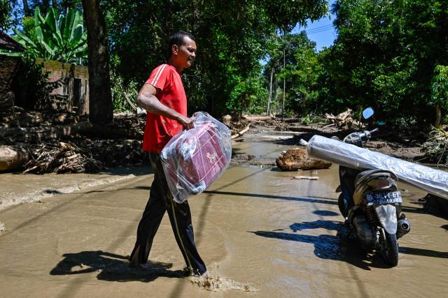 A man carries belongings in a flooded area in Meureudu, Pidie Jaya district in Indonesia's Aceh province on November 30, 2025. The death toll from floods that hit Indonesia this week has risen to more than 300 people, according to figures from the disaster agency on November 29. (Photo by CHAIDEER MAHYUDDIN / AFP)