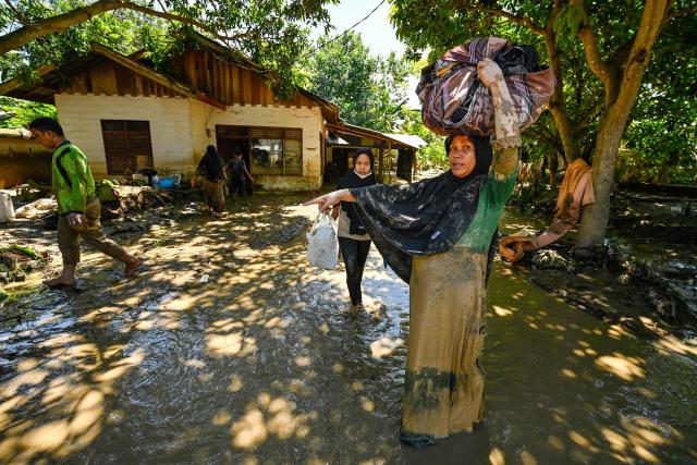 A woman carries belongings in a flooded area in Meureudu, Pidie Jaya district in Indonesia's Aceh province on November 30, 2025. The death toll from floods that hit Indonesia this week has risen to more than 300 people, according to figures from the disaster agency on November 29. (Photo by CHAIDEER MAHYUDDIN / AFP)