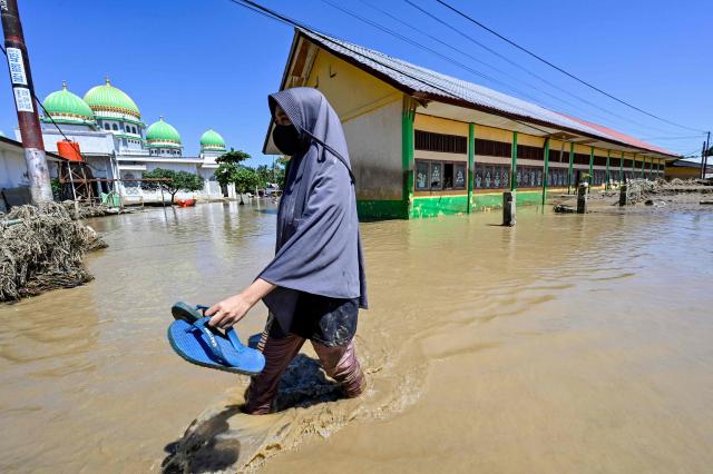 A woman walks past a mosque in a flooded area in Meureudu, Pidie Jaya district in Indonesia's Aceh province on November 30, 2025. The death toll from floods that hit Indonesia this week has risen to more than 300 people, according to figures from the disaster agency on November 29. (Photo by CHAIDEER MAHYUDDIN / AFP)