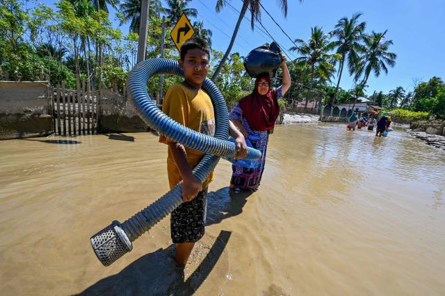 People walk in a flooded area in Meureudu, Pidie Jaya district in Indonesia's Aceh province on November 30, 2025. The death toll from floods that hit Indonesia this week has risen to more than 300 people, according to figures from the disaster agency on November 29. (Photo by CHAIDEER MAHYUDDIN / AFP)
