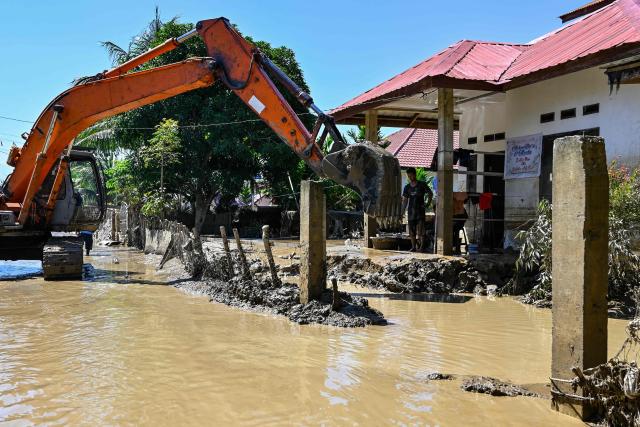 An excavator clears mud surrounding a house amid flooding in Meureudu, Pidie Jaya district in Indonesia's Aceh province on November 30, 2025. The death toll from floods that hit Indonesia this week has risen to more than 300 people, according to figures from the disaster agency on November 29. (Photo by CHAIDEER MAHYUDDIN / AFP)