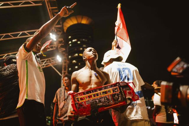 A member of Kenyan artist Parroty Vunulu’s team holds a miniature matatu -Kenya’s iconic, privately owned public transport minibus- during a performance for the 4th Nganya Awards  in Nairobi on November 29, 2025. The Nganya Awards is a celebration of Kenya’s matatu culture, honoring the matatu scene and the unique lifestyle around them. This years awards had over 40 categories, from matatu crews to vehicle designers, sound system and social influencers linked to the matatu lifestyle, with voting taking place ahead of the award show. (Photo by Fredrik LERNERYD / AFP)