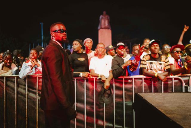 A security guard stands by the stage as fans follow the party during the 4th Nganya Awards celebrating matatu culture -Kenya’s iconic, privately owned public transport minibus- in Nairobi on November 29, 2025. The Nganya Awards is a celebration of Kenya’s matatu culture, honoring the matatu scene and the unique lifestyle around them. This years awards had over 40 categories, from matatu crews to vehicle designers, sound system and social influencers linked to the matatu lifestyle, with voting taking place ahead of the award show. (Photo by Fredrik LERNERYD / AFP)