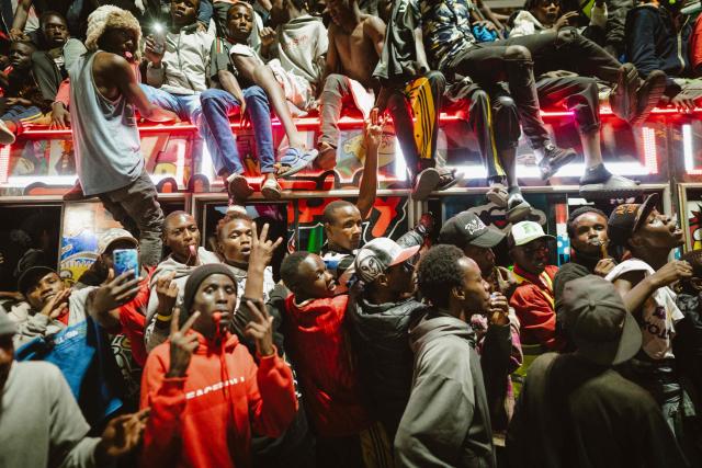 A group of fans rides atop a matatu -Kenya’s iconic, privately owned public transport minibus- driving around the venue as fans gather for the 4th Nganya Awards in Nairobi on November 29, 2025. The Nganya Awards is a celebration of Kenya’s matatu culture, honoring the matatu scene and the unique lifestyle around them. This years awards had over 40 categories, from matatu crews to vehicle designers, sound system and social influencers linked to the matatu lifestyle, with voting taking place ahead of the award show. (Photo by Fredrik LERNERYD / AFP)
