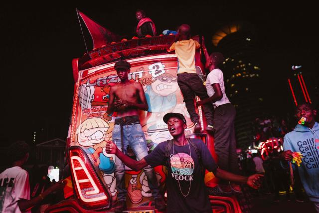 A group of fans climbs atop a matatu -Kenya’s iconic, privately owned public transport minibus- driving around the venue as fans gather for the 4th Nganya Awards in Nairobi on November 29, 2025. The Nganya Awards is a celebration of Kenya’s matatu culture, honoring the matatu scene and the unique lifestyle around them. This years awards had over 40 categories, from matatu crews to vehicle designers, sound system and social influencers linked to the matatu lifestyle, with voting taking place ahead of the award show. (Photo by Fredrik LERNERYD / AFP)