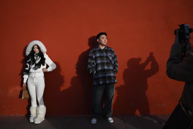 People pose for pictures in an area popular with tourists in Beijing on November 30, 2025. (Photo by Pedro PARDO / AFP)