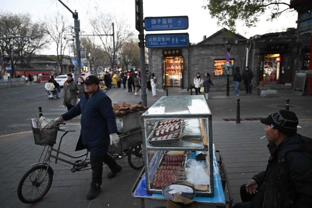 Street food vendors wait for customers in an area popular with tourists in Beijing on November 30, 2025. (Photo by Pedro PARDO / AFP)