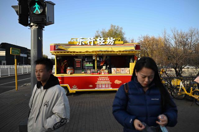 People stand in front of a food truck in an area popular with tourists in Beijing on November 30, 2025. (Photo by Pedro PARDO / AFP)