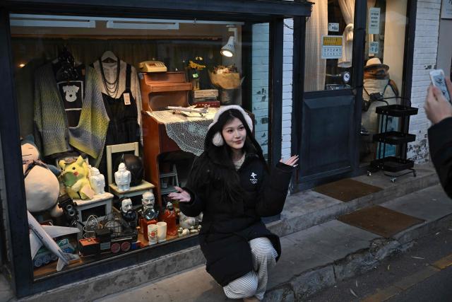 A woman poses for pictures in front of a store in an area popular with tourists in Beijing on November 30, 2025. (Photo by Pedro PARDO / AFP)