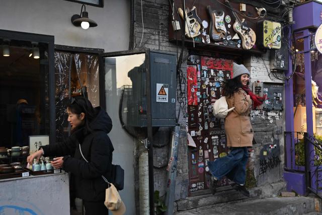A woman jumps as she poses for pictures in front of a store in an area popular with tourists in Beijing on November 30, 2025. (Photo by Pedro PARDO / AFP)