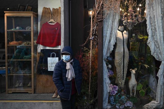A woman stands in front of a store in an area popular with tourists in Beijing on November 30, 2025. (Photo by Pedro PARDO / AFP)
