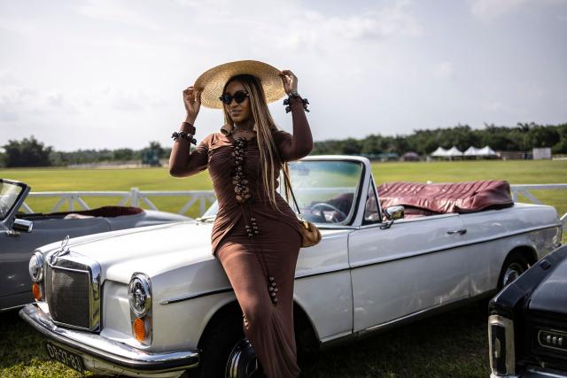 A spectator poses with a classic car exhibited during the Isimi Festival 2025 at the Isimi Wellness and Polo Country Estate in Epe, Lagos State, on November 29, 2025. (Photo by OLYMPIA DE MAISMONT / AFP)