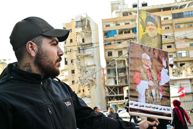 A man holds a poster of Pope Leo XIV that reads "Welcome to the Dahiyeh of Sayyed Nasrallah", referring to assassinated Hezbollah leader Hassan Nasrallah (seen in poster above), in Beirut's southern suburbs, a packed residential area known as Dahiyeh, which is also a Hezbollah bastion, on November 30, 2025, as crowds gather ahead of the Popes arrival. Pope Leo XIV is heading to Lebanon with a message of peace for the crisis-hit nation after wrapping up a four-day trip to Turkey's tiny Christian community that focused on unity within the Church. (Photo by Giuseppe CACACE / AFP)