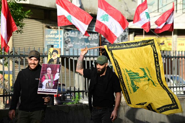 Lebanese men hold a poster of Pope Leo XIV that reads "Welcome to the Dahiyeh of Sayyed Nasrallah", referring to assassinated Hezbollah leader Hassan Nasrallah (seen in poster above), and a Hezbollah flag in Beirut's southern suburbs, a packed residential area known as Dahiyeh, which is also a Hezbollah bastion, on November 30, 2025. Pope Leo XIV is heading to Lebanon with a message of peace for the crisis-hit nation after wrapping up a four-day trip to Turkey's tiny Christian community that focused on unity within the Church. (Photo by Giuseppe CACACE / AFP)