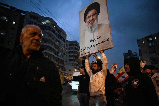 A man holds a portrait of assassinated Hezbollah leader Hassan Nasrallah as the convoy of Pope Leo XIV drives through Beirut's southern suburbs, a packed residential area known as Dahiyeh, which is also a Hezbollah bastion, on November 30, 2025. Pope Leo XIV arrived in Lebanon on November 30 with a message of peace for the crisis-hit nation, still reeling from a war between Israel and Hezbollah and the conflict's lingering aftereffects. (Photo by JOSEPH EID / AFP)