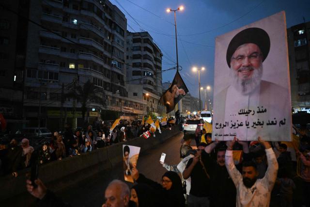 TOPSHOT - People hold posters of assassinated Hezbollah leader Hassan Nasrallah as the convoy of Pope Leo XIV drives through Beirut's southern suburbs, a packed residential area known as Dahiyeh, which is also a Hezbollah bastion, on November 30, 2025. Pope Leo XIV arrived in Lebanon on November 30 with a message of peace for the crisis-hit nation, still reeling from a war between Israel and Hezbollah and the conflict's lingering aftereffects. (Photo by JOSEPH EID / AFP)