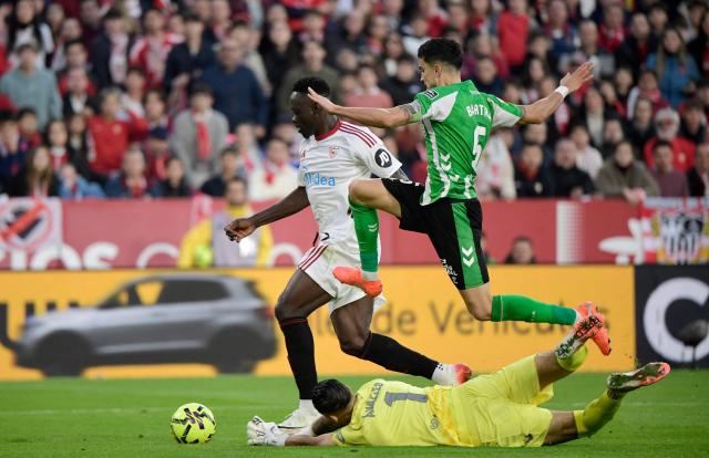 Sevilla's Nigerian forward #09 Akor Jerome Adams fights for the ball with with Real Betis' Spanish defender #05 Marc Bartra and Real Betis' Spanish goalkeeper #01 Alvaro Valles during the Spanish league football match between Sevilla FC and Real Betis at Ramon Sanchez Pizjuan Stadium in Seville on November 30, 2025. (Photo by CRISTINA QUICLER / AFP)