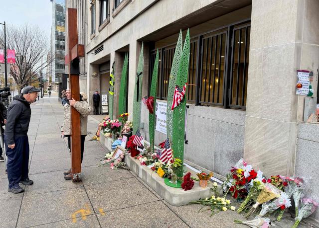 A man holds an oversized cross while visiting a makeshift memorial for the two National Guard members who were shot near the White House, in Washington, DC, November 30, 2025. Two National Guard troops, Staff Sgt. Andrew Wolfe and Specialist Sarah Beckstrom, were shot on November 26 near the White House in what authorities described as a targeted attack by an Afghan migrant who had previously worked with the US military in Afghanistan, a case now being treated as a terrorism investigation. (Photo by Daniel SLIM / AFP)