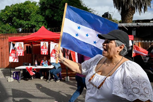 A woman waves a Honduran flag near a polling station during the general election in Tegucigalpa on November 30, 2025. Hondurans voted for president on Sunday amid threats by US President Donald Trump to cut aid to the country if his preferred candidate loses. (Photo by Orlando SIERRA / AFP)