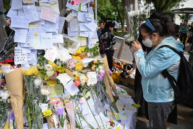 A mourner pays her respects for victims at a makeshift memorial outside the Wang Fuk Court apartment blocks in the aftermath of the deadly November 26 fire in Hong Kong's Tai Po district on December 1, 2025. Police as well as Hong Kong's anti-corruption watchdog have launched investigations into the blaze that have killed at least 146 people, but a petition calling for greater accountability and demanding an independent probe was swiftly shut down as an organiser was reportedly arrested for sedition. (Photo by Peter PARKS / AFP)