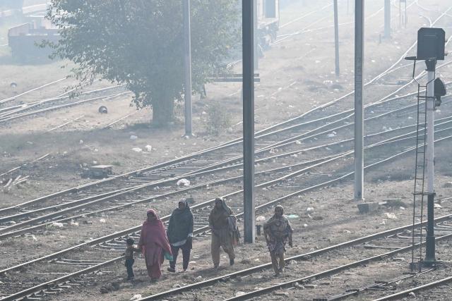 Women with a child walk along railway tracks strewn with garbage amid dense smog in Lahore on December 1, 2025. (Photo by Arif ALI / AFP)