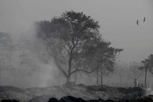 TOPSHOT - A man walks past burning garbage along a roadside amid dense smog in Lahore on December 1, 2025. (Photo by Arif ALI / AFP)