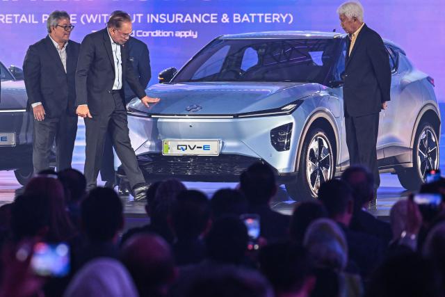 Malaysia's Prime Minister Anwar Ibrahim (2nd L) touches the exterior of Perodua's first EV car during a launch event in Kuala Lumpur on December 1, 2025. (Photo by Mohd RASFAN / AFP)