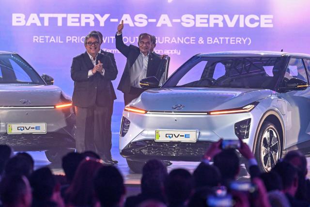 Malaysia's Prime Minister Anwar Ibrahim (C) gives a thumbs up next to Perodua's first EV car during a launch event in Kuala Lumpur on December 1, 2025. (Photo by Mohd RASFAN / AFP)