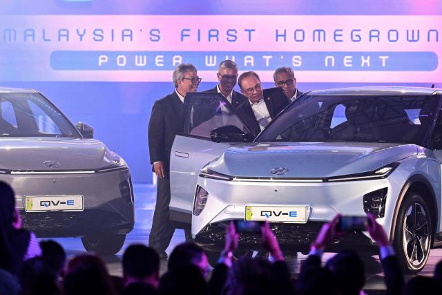 Malaysia's Prime Minister Anwar Ibrahim (C) gets inside Perodua's first EV car during a launch event in Kuala Lumpur on December 1, 2025. (Photo by Mohd RASFAN / AFP)