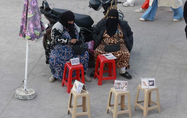 Women who create henna tattoos, sit waiting for customers in Jemaa el-Fna Square or Jamaa Lafna, listed as UNESCO Cultural Heritage site, located in the heart of the Medina of the city of Marrakech on November 30, 2025. (Photo by Abdel Majid BZIOUAT / AFP)