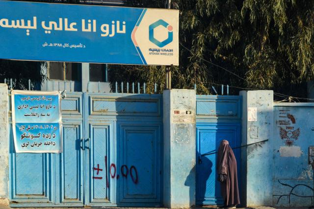 An Afghan burqa-clad woman waits to enter a school in Kandahar on December 1, 2025. (Photo by Sanaullah SEIAM / AFP)