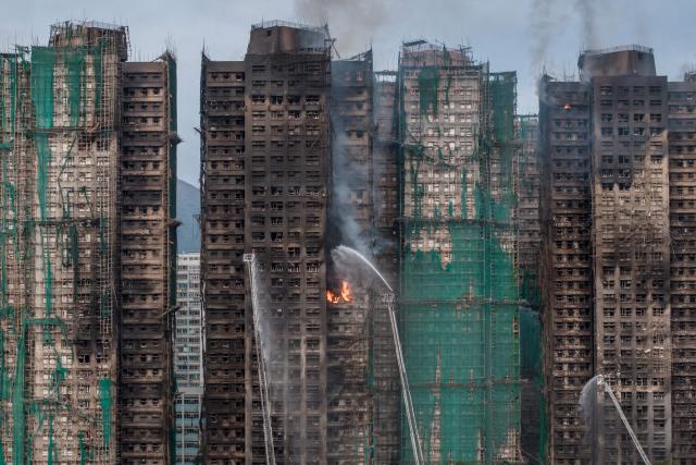 (FILES) Smoke rises from apartments after a major fire swept through several blocks at the Wang Fuk Court residential estate in Hong Kong's Tai Po district on November 27, 2025. Hong Kong police said on December 1 they had arrested a total of 13 people for manslaughter over a deadly fire that ripped through an apartment complex last week, killing at least 146. (Photo by Dale DE LA REY / AFP)
