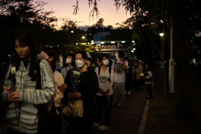 (FILES) People line up to offer flowers outside the Wang Fuk Court in the aftermath of the deadly November 26 fire in Hong Kong's Tai Po district on November 29, 2025. Hong Kong police said on December 1 they had arrested a total of 13 people for manslaughter over a deadly fire that ripped through an apartment complex last week, killing at least 146. (Photo by Philip FONG / AFP)