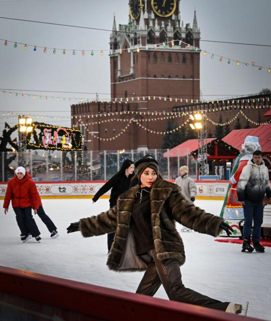 People enjoy skating at a temporary open air ice rink in the center of Red Square, with the Kremlin's Spasskaya Tower seen in the background, in Moscow on December 1, 2025. (Photo by Alexander NEMENOV / AFP)